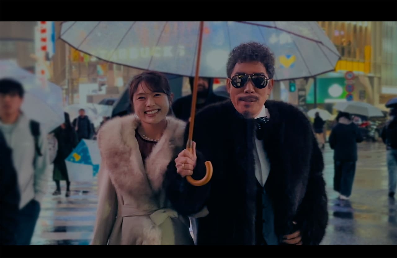 鈴木雅之「渋谷で5時（2026 Ver.）feat. 渋谷凪咲」ミュージックビデオより。渋谷駅前のスクランブル交差点で相合傘をしながらほほえむ2人。