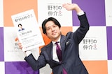 “に野村和也”の巨大名刺を持ってムービーカメラにアピールする二宮和也。
