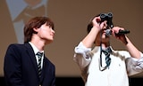 観客から借りた双眼鏡を使用する清水海李（右）に興味津々な桜木雅哉（原因は自分にある。 / 右）。ファンミーティング「修学旅行で仲良くないグループに入りました～夏休み同窓会～」より。