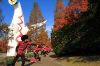 太陽の塔をバックに練り歩く謎の16人。写真は実際の写真集には含まれていないアザーカット。(c)吉本興業