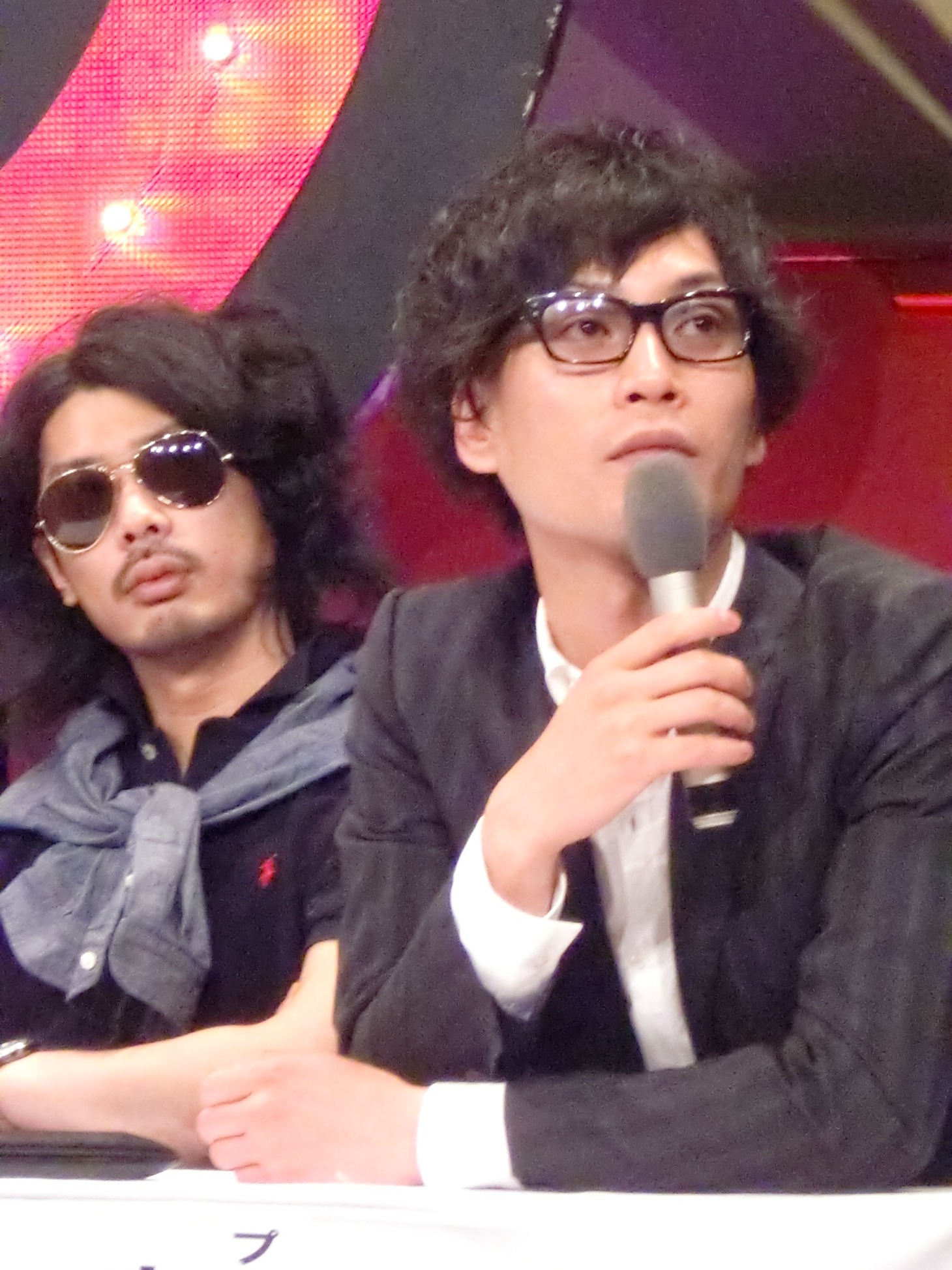 次々と手を挙げ質問をしようとする竹内記者と武山記者に冷めた視線を送る安達プロデューサーと菅オーナー。
