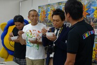 「LIVE STAND 2010」の飲食ブースに「炭火焼肉たむら」を出店していたたむらけんじが、タカアンドトシとCOWCOWよしに試食させている様子。