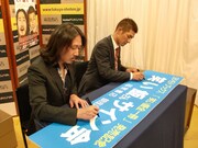 「笑い飯さんサイン会」の看板にサインをする2人。
