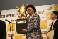 日本バナナ輸入組合イメージキャラクター「バナピィ」をかたどったトロフィーを受け取った日村。