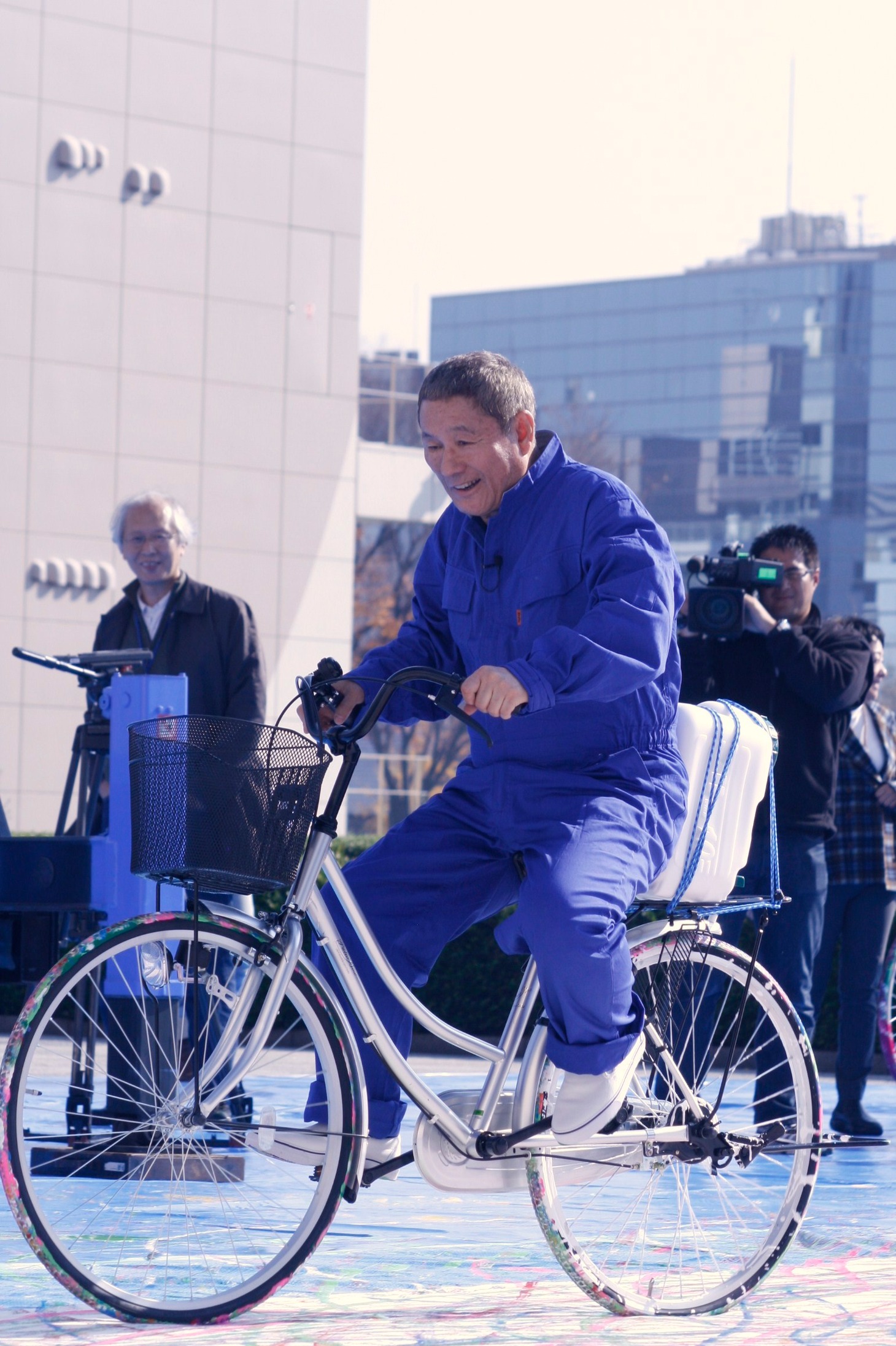 白色のアクリル絵の具を搭載した自転車に自らまたがり、ペイントを行うたけし。