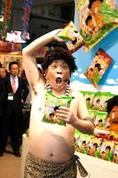 「JCC アダモちゃんスナック 新商品発表会」に登場したアダモちゃんこと島崎俊郎。右手に「ステーキ風味」、左手に「サラダ風味」を持っている。