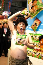 「JCC アダモちゃんスナック 新商品発表会」に登場したアダモちゃんこと島崎俊郎。右手に「ステーキ風味」、左手に「サラダ風味」を持っている。