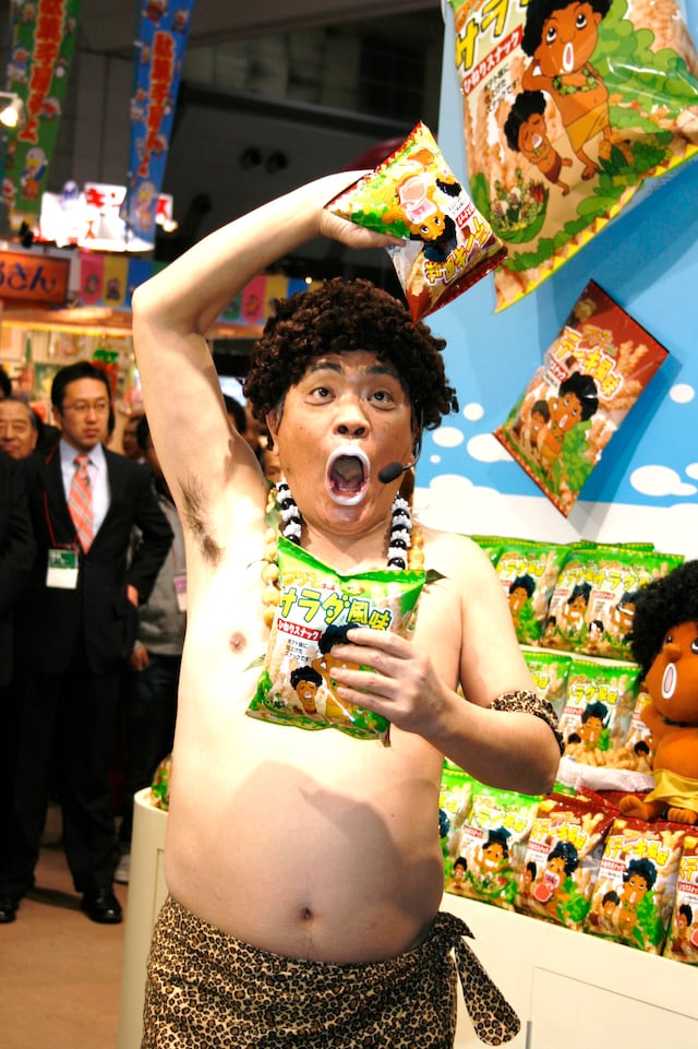 「JCC アダモちゃんスナック 新商品発表会」に登場したアダモちゃんこと島崎俊郎。右手に「ステーキ風味」、左手に「サラダ風味」を持っている。