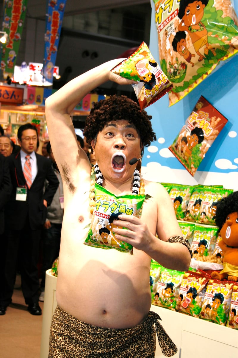 「JCC アダモちゃんスナック 新商品発表会」に登場したアダモちゃんこと島崎俊郎。右手に「ステーキ風味」、左手に「サラダ風味」を持っている。