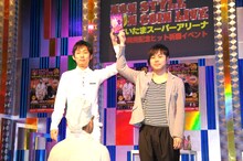 DVDを掲げるNON STYLEの2人と、彼らの前にひざまずいて祈りを捧げたオネエ祈祷師・びびこ（手前）。