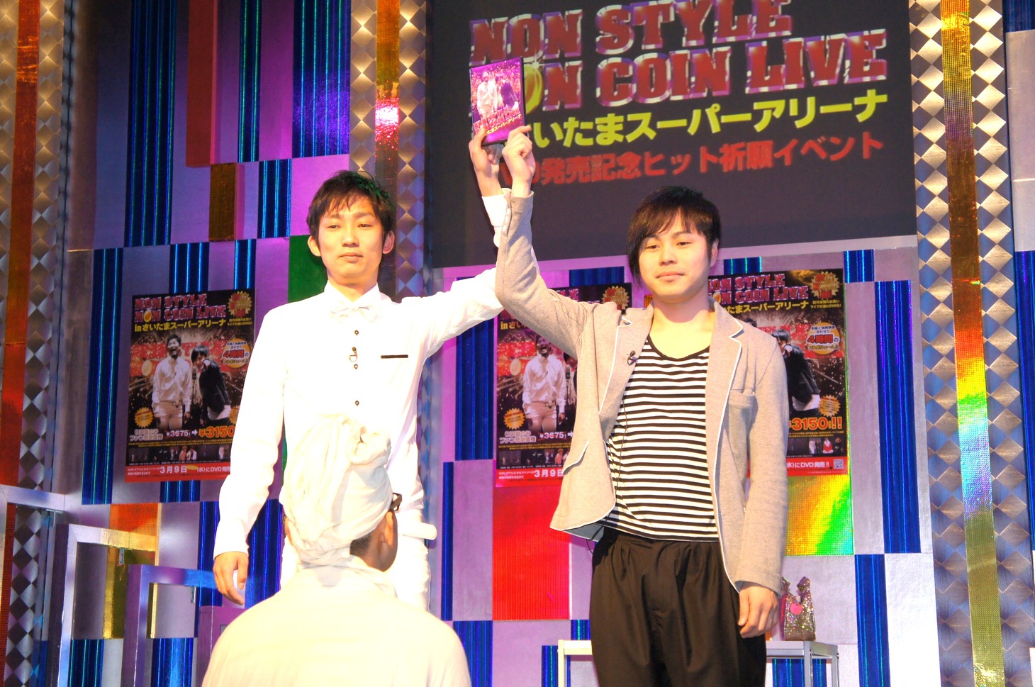 DVDを掲げるNON STYLEの2人と、彼らの前にひざまずいて祈りを捧げたオネエ祈祷師・びびこ（手前）。