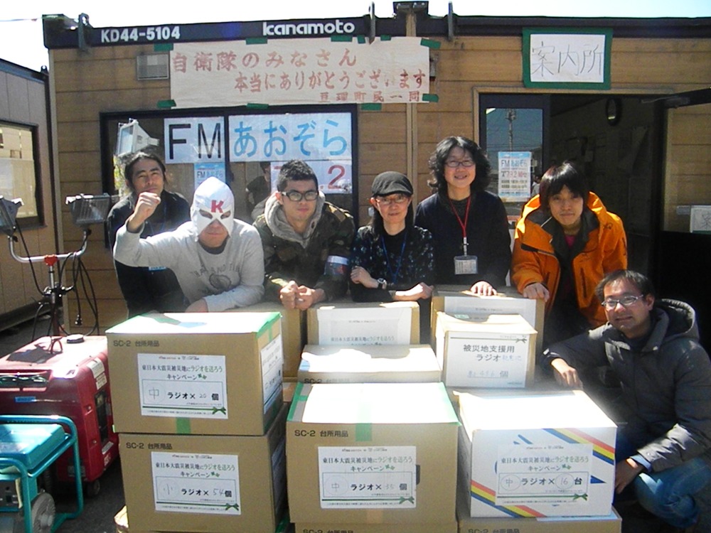 宮城県・亘理町の臨時災害放送局「FMあおぞら」を訪問し、ラジオ1000台と乾電池を寄贈した小島よしお（左から3人目）ら。
