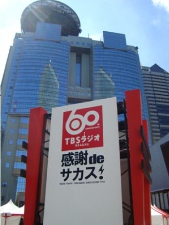 「TBSラジオ開局60周年記念イベント『感謝 de サカス！』」のロゴとTBS放送センター（ビッグハット）。