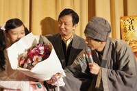 嶋田瑠那（左）に花束を贈呈する次長課長・井上（右）。中央は通訳。