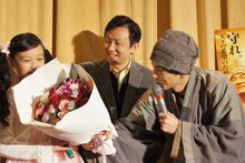 嶋田瑠那（左）に花束を贈呈する次長課長・井上（右）。中央は通訳。