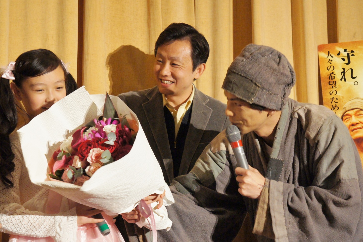 嶋田瑠那（左）に花束を贈呈する次長課長・井上（右）。中央は通訳。