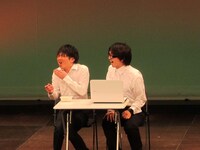 有名ハガキ職人に会えて喜ぶ佐藤。辻本はラジオのノベルティの定規で同じくノベルティの豆腐を食べている。