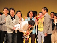 受賞は日刊スポーツより。舞台上で行われた記念撮影では新宿カウボーイ・かねきよが写り込もうと必死に。