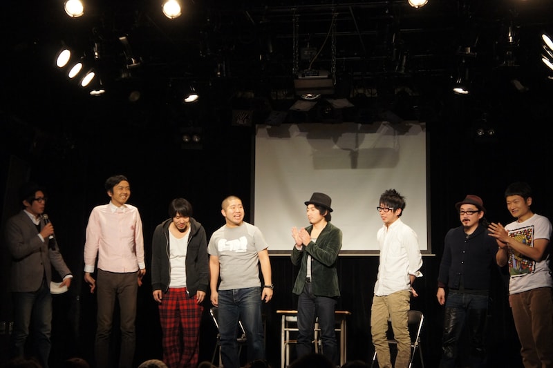 「ワタナベvsスラッシュパイル『ゲームセンター 表参道店』」の一場面。ザブングル松尾（左端）MCのもと、7名の芸人がゲーム対決を繰り広げた。