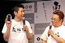 「でっかくなっちゃった！」の耳が実はiPhoneケースだったことを明かすマギー審司（左）。