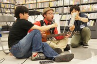 タワーレコード秋葉原店のフロアにあぐらをかき、レアな楽曲をギター弾き語りで披露するマキタスポーツ（中央）。