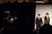 ザンゼンジ岡野を狙撃するべく、客席からステージへ銃を構える鬼ヶ島・おおかわら（左）。