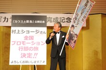 「全国プロモーション行脚中」ののぼりを手にする村上ショージ。