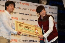 副賞でジーンズメイト5万円分の商品券を受け取ったライセンス藤原（右）。