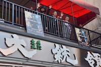 居酒屋「大統領」の2階から街の人々に手を振る3人。