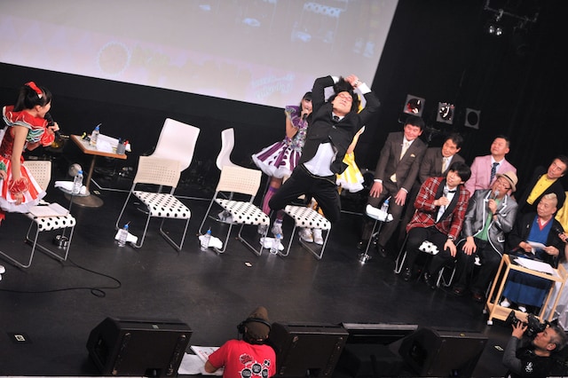 ももいろクローバーZのトークイベント「ももクロ試練の七番勝負 episode.3」の第7戦「VS.浅草」で、柳家松太郎の切り絵の参考にするため、百田夏菜子（左端）の「えびぞりジャンプ」を代理で実演する南海キャンディーズ山里（中央）。