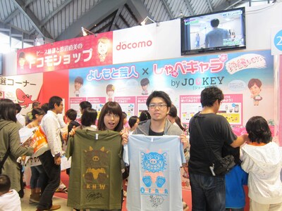 「第5回沖縄国際映画祭」ラフピータウン・JOOKEYブース。写真はお笑いナタリー読者にプレゼントTシャツを進呈したNTTドコモの広瀬氏、佐藤氏（左から）。