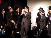 罰ゲーム執行人から封筒を渡されるピテカントロプス（左）。