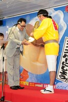「凍らせプッチンプリン大使就任イベント」で金色の特大凍らせプッチンバーを授与されるますだおかだ岡田（右）。