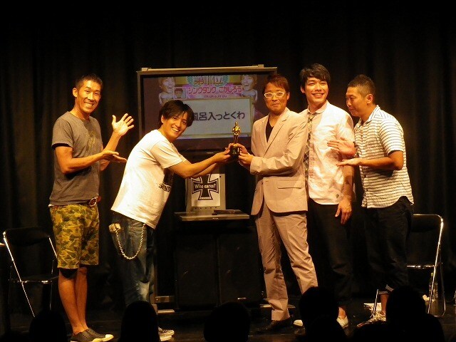 「誰が興味あんねんツイート大賞2013上半期」大賞を受賞したこかじろうにトロフィーを渡す主催のザ・プラン9のヤナギブソン。