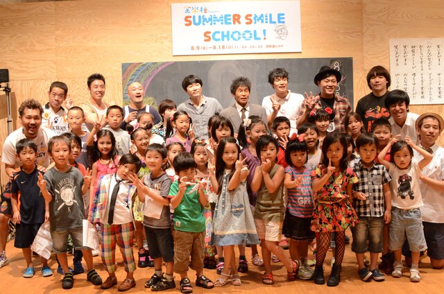 「笑楽校 presents SUMMER SMILE SCHOOL」の特別授業「みんなで校歌を作ろう！」終了後に、みんなで記念撮影。ゲストのHARCO先生、MCのタケト、間寛平校長、山田花子教頭のほか、期間中に授業を実施する予定のFUJIWARA、くまだまさし、なかやまきんに君、チーモンチョーチュウ、エハラマサヒロ、もう中学生が参加した。