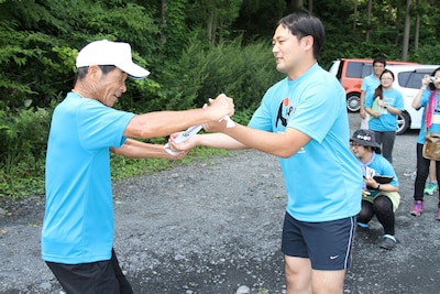 第2走者のアンダーエイジ結城（右）にタスキを渡す間寛平。