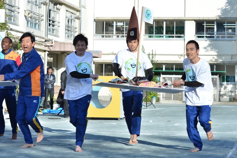 「DeNA Sekai☆Egao Project はだしランイベント」にて、裸足で校庭を走る、かもめんたると小島よしお（中央）。手前左は石田純一。