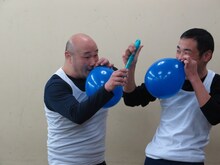 スマホ向けオークションサービス「パシャオク」の「えがお∞（むげんだい）プロジェクト」に「くまだまさしとコラボギャグをやれる！ DVD収録付き」を出品したくまだまさし（左）と、その落札者（右）。