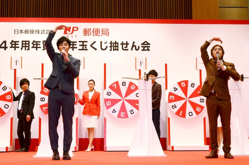 「立会人」として、ルーレットに刺さった矢の番号を確認し、「まる」のジェスチャーで承認するキングコング（手前）。