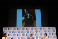 「増税前節約トークショー Presented by Wi-Fi ほぼスマホ」の様子。スクリーンには東貴博の自宅にある「座ると優勝する」ジンクスを持つ“キングのイス”に座るやまもとの姿が映し出された。