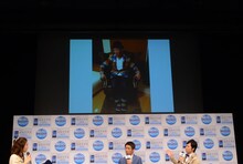 「増税前節約トークショー Presented by Wi-Fi ほぼスマホ」の様子。スクリーンには東貴博の自宅にある「座ると優勝する」ジンクスを持つ“キングのイス”に座るやまもとの姿が映し出された。