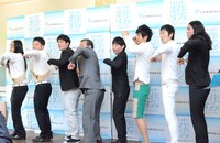 「せーの！ ワクワク！」とプロジェクトの5か条を紹介する芸人たちに混ざる大久保市長（左から4人目）。