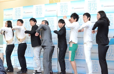 「せーの！ ワクワク！」とプロジェクトの5か条を紹介する芸人たちに混ざる大久保市長（左から4人目）。