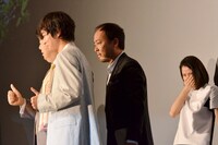 帽子を取って舞台挨拶中の記念撮影にフレームインするマキタスポーツ（中央）。