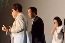 帽子を取って舞台挨拶中の記念撮影にフレームインするマキタスポーツ（中央）。