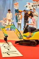 小型のショベルカーを操縦して書道に挑む、ハリセンボンはるか（手前）。