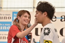 フットサル大会「uno cup」のPRイベントで、リフティング対決を制したご褒美としてマギー（左）に顔の汗を拭いてもらう、ライセンス井本（右）。