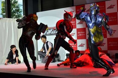 仮面ライダードライブが悪役を蹴散らすのを見守る土田晃之（後方中央）。