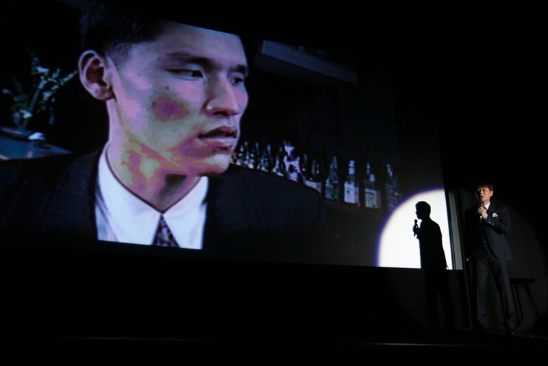 映画「ベイブルース～25歳と364日～」の舞台挨拶で、河本栄得の映像を流しながらネタを披露する高山トモヒロ監督（右）。
