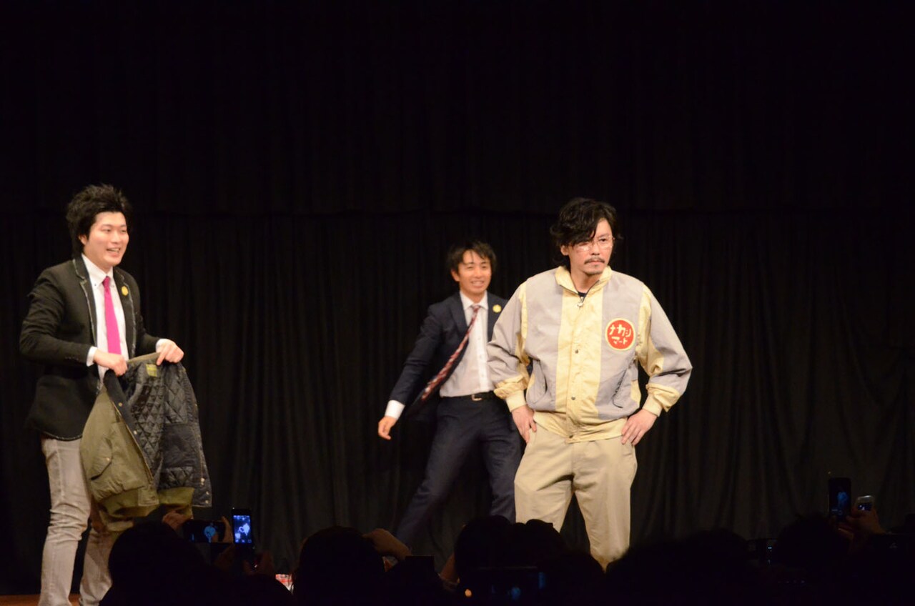 ファンに向かってポーズを決めるマツモトクラブ（手前）と着替えを手伝う湘南デストラーデ。